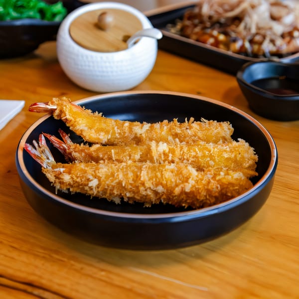 Crispy golden-brown shrimp tempura in a black bowl on a wooden table at Hikari Ramen.