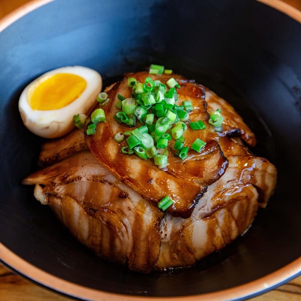 Hikari Ramen's chashu pork with green onions and a soft-boiled egg in a black bowl.