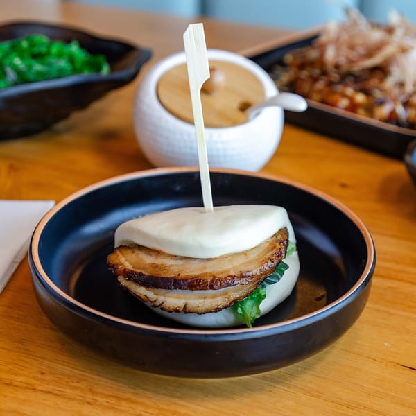 A Hikari Ramen pork belly bao bun with lettuce, served in a black bowl.