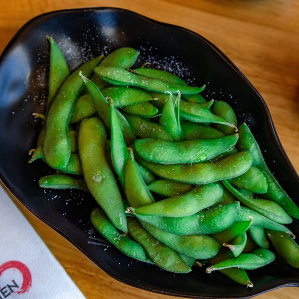 A black bowl filled with vibrant green edamame pods, lightly sprinkled with sea salt.